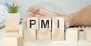 Text PMI on wood cube with gold bar and newspaper on the table