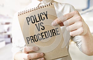 Text POLICY VS PROCEDURE on brown paper notepad in businessman hands in office. Business concept