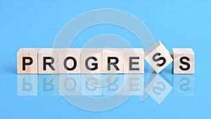 The text PROGRESS is written on the cubes in black letters, the cubes are located on a blue glass surface