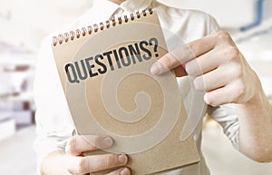Text QUESTIONS on brown paper notepad in businessman hands in office. Business concept