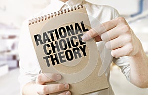 Text RATIONAL CHOICE THEORY on brown paper notepad in businessman hands in office. Business concept