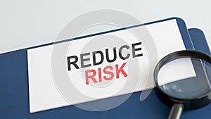 text reduce risk on white paper card, black ahd red letters. lens on blue background. business concept. education