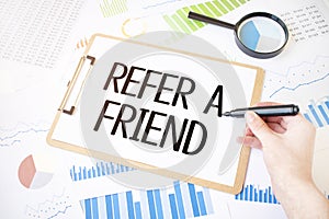 Text REFER A FRIEND on white paper sheet and marker on businessman hand on the diagram. Business concept