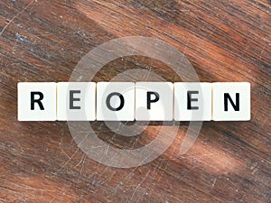 Text reopen made of square letter tiles on wooden background.