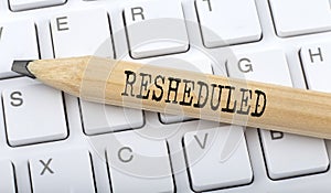 Text RESHEDULED on wooden pencil on white keyboard. Business concept photo