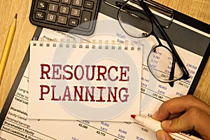 The text RESOURCE PLANNING is written on a white folded sheet of paper on the table.