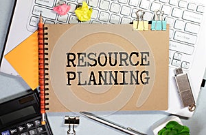 The text RESOURCE PLANNING is written on a white folded sheet of paper on the table