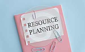 The text RESOURCE PLANNING is written on a white folded sheet of paper on the table. Nearby are pens and pencils