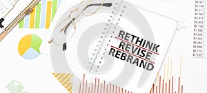 Text RETHINK REVISE REBRAND on white notepad, glasses, graphs and diagrams
