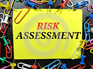 Text RISK ASSESSMENT on color paper with paper clips and pinboards on black background.