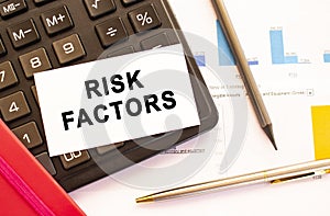 Text RISK FACTORS on white card with metal pen, calculator and financial charts
