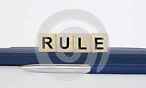 The text Rule on a wooden cubes, lying on a Notepad with a metal blue pen