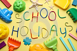 Text School Holidays made of modelling clay and different sand toys on background, flat lay