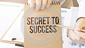 Text Secret to Success on brown paper notepad in businessman hands on the table with diagram. Business concept