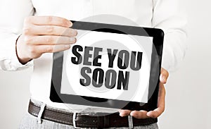 Text SEE YOU SOON on tablet display in businessman hands on the white background. Business concept