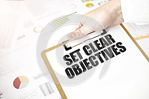 Text SET CLEAR OBJECTIVES on white paper plate in businessman hands with financial diagram. Business concept