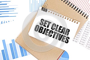 Text SET CLEAR OBJECTIVES on white paper sheet and brown paper notepad on the table with diagram. Business concept