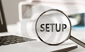 Text SETUP on magnifying glass on an office desk. Business concept for the analysisner, position, or direction in which something photo