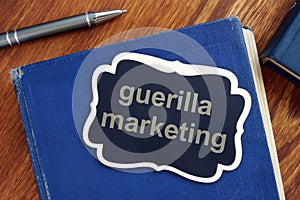 Text sign showing guerilla marketing. The text is written on a small wooden blackboard. The book, pen, wooden background are on photo