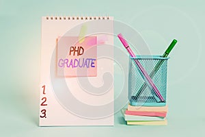 Text sign showing Phd Graduate. Conceptual photo highest university degree that is conferred after a course Spiral notebook sticky