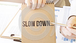 Text slow down on brown paper notepad in businessman hands on the table with diagram. Business concept