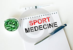 Text Sport Medecine written in a notebook with a blue pen and a bunch of pills