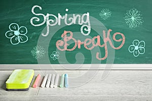 Text Spring Break and flower drawings on green chalkboard near wooden table. School holiday