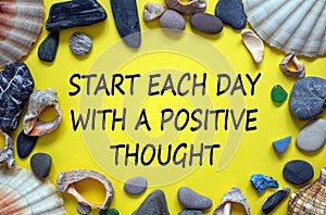 Text `start each day with a positive thought` on a beautiful yellow background. Sea stones and seashells. Concept