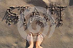 Text start written in sand on sea beach and womans bare feet