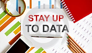 Text STAY UP TO DATA on the notepad with office tools, pen on financial report