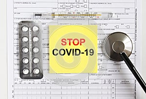 Text Stop Covid-19 on yellow sticker with a stethoscope and pills are on medical documents