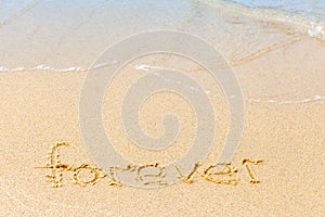 Text on a sunny beach. The word Forever written by hand in the sand, washed away by the sea wave. The concept of irony