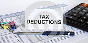 Text Tax Deductions on white card with blue metal pen, calculator and paper clips on financial table