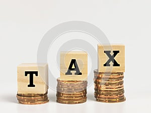 Text TAX on wooden cubes with stacked coins.