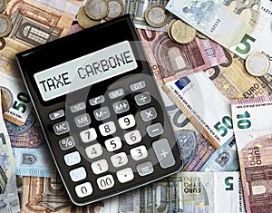 Text TAXE CARBONE, French for carbon tax, on display of pocket calculator against euro bills on table