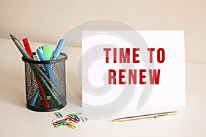 The text TIME TO RENEW is written on a white folded sheet of paper on the table. Nearby are pens and pencils.