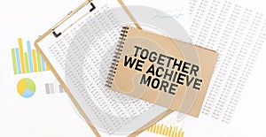 Text TOGETHER WE ACHIEVE MORE on brown paper notepad on the table with diagram. Business concept