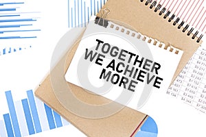 Text TOGETHER WE ACHIEVE MORE on white paper sheet and brown paper notepad on the table with diagram. Business concept