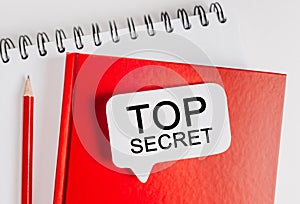 Text Top Secret on a white sticker on red notepad with office stationery background. Flat lay on business, finance and development