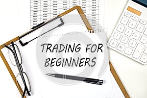 Text TRADING FOR BEGINNERS on the white paper on clipboard with chart and calculator