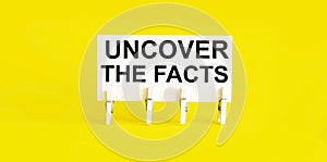 Text UNCOVER THE FACTS on white short note paper yellow background