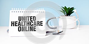 The text UNITED HEALTHCARE ONLINE is written on notepad near a stethoscope on a blue background. Medical concept