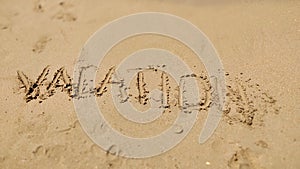 Text Vacation written in the sand of sea beach