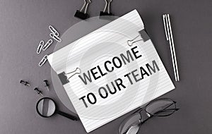 Text WELCOME TO OUR TEAM on Notebook and office tools on the gray desktop