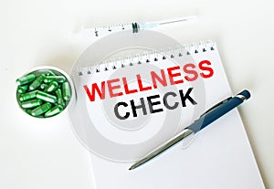 Text Wellness Check written in a notebook with a blue pen and a bunch of pills