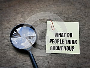 text What do people think about you on sticky note with magnifying glass on wooden background.