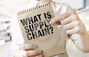 Text WHAT IS SUPPLY CHAIN on brown paper notepad in businessman hands in office. Business concept