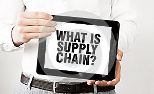 Text WHAT IS SUPPLY CHAIN on tablet display in businessman hands on the white background. Business concept