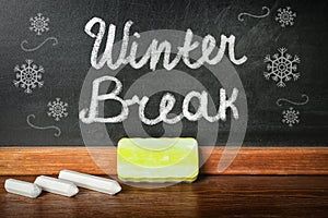 Text Winter break and snowflakes on school blackboard near table with chalk and duster