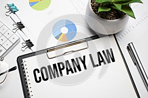 Text, the word COMPANY LAW is written in a notebook lying on a black table with a pen, glasses and a calculator. Business concept